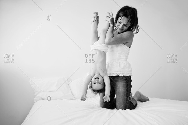 Mother holding her laughing baby upside down on bed