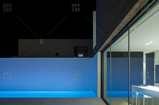 Swimming pool casts a blue glow against white stucco wall at night
