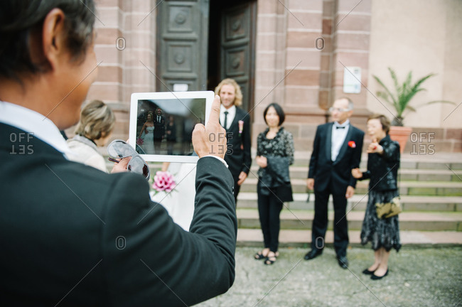 Guest taking a wedding group photo with a digital tablet on the stairs of the church
