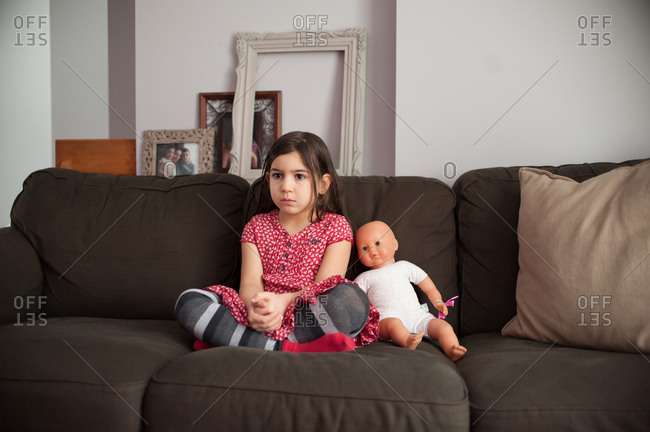 Child sitting on the couch with her doll watching television