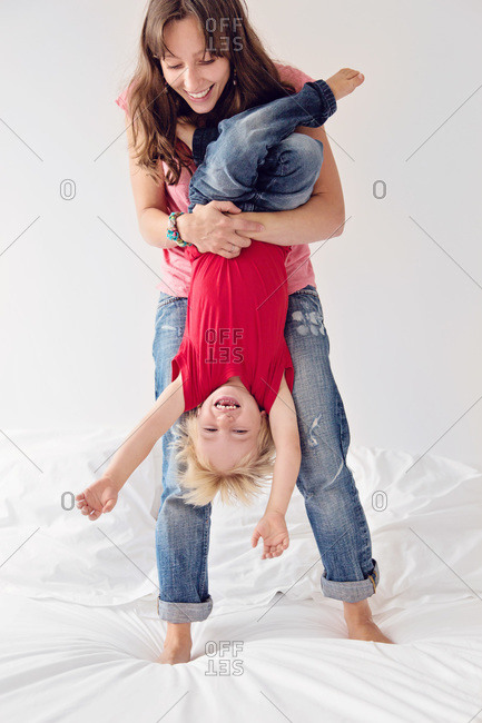 A mom holds her son upside-down on a bed