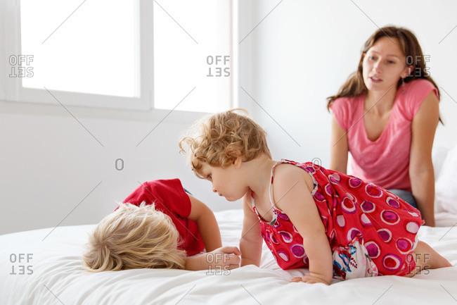 A little girl and her brother lay with their mom on a bed
