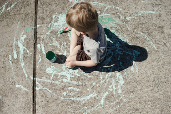 Boy sitting painting on driveway from above