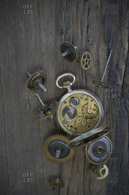 Old pocket watch and cogwheels on dark wood