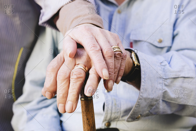 Close-up of old man\'s and woman\'s hands resting on a cane