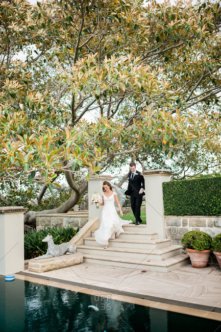 Bride and groom descending stairs by an outdoor fountain