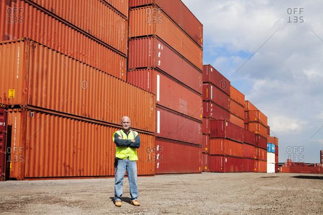 Employee with arms crossed in front of freight containers