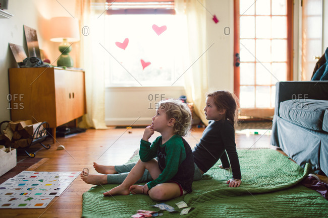 A brother and sister watch television together on the living room floor
