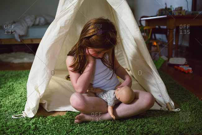 A little girl plays with a baby doll in an indoor tent