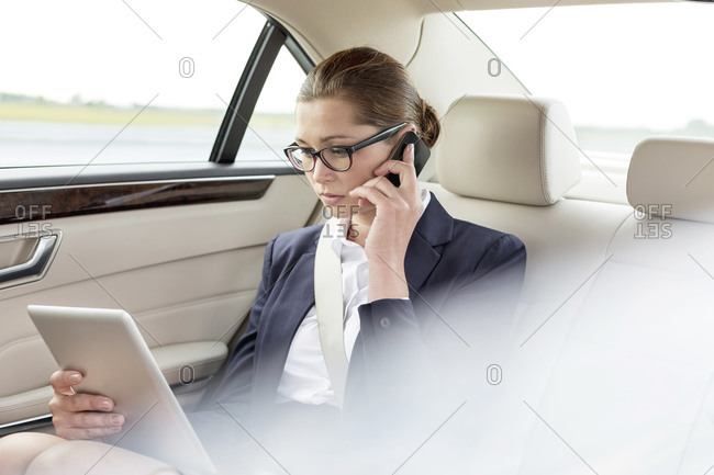 Businesswoman with cell phone and digital tablet in back seat of a car