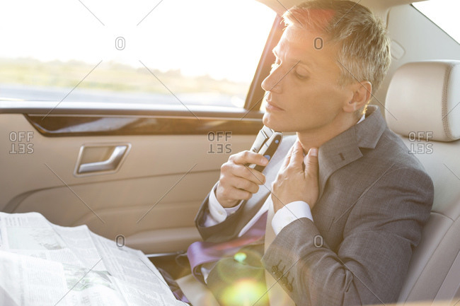 Businessman reading newspaper and shaving in car