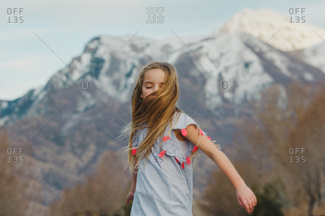 A little girl spins around in front of snowcapped mountains
