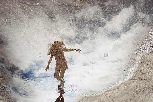 Young girl reflected in a puddle on pavement