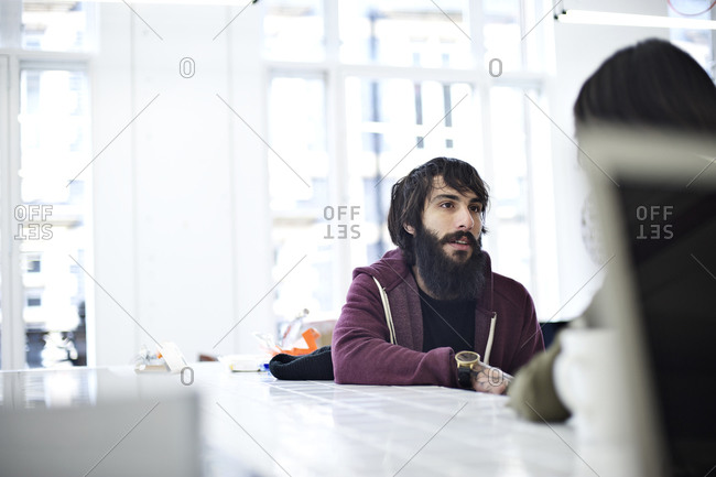 Bearded man in hoodie talking to co-worker at a conference table