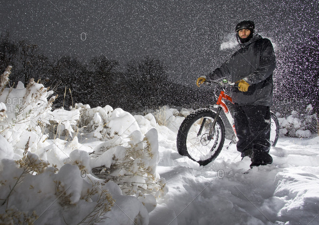 Man stands with fat tire bike while heavy snow falls