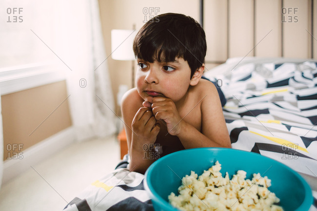 Boy laying on bed with bowl of popcorn