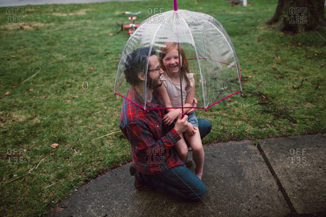A little girl and her dad giggle under a bucket umbrella
