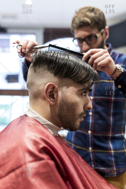 Hairdresser parting a young man\'s hair in a barbershop