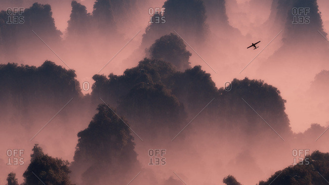 A small airplane flies through misty mountaintops in pink evening light