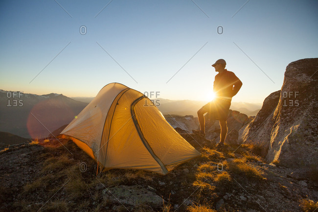 A silhouetted hiker partially blocks the sunset while camping on Saxifrage Peak, Pemberton, BC, Canada