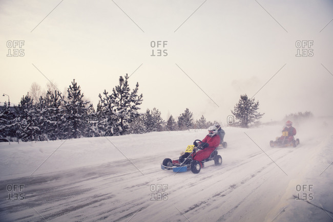 Three drivers racing go-karts on a snow covered track