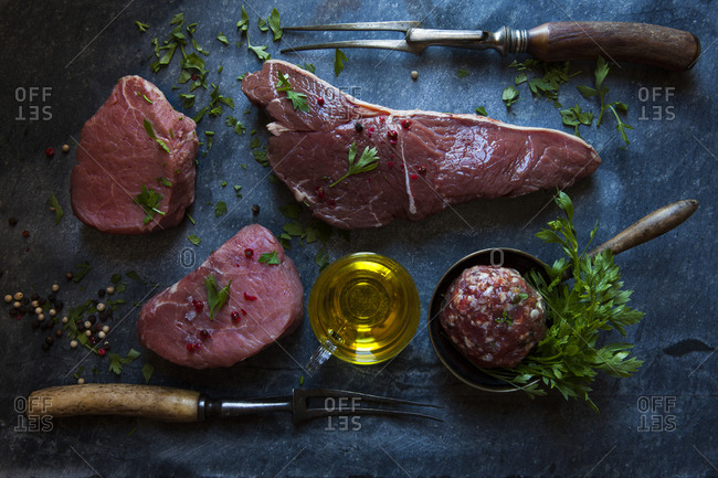 Cuts of meat with herbs on a slate background