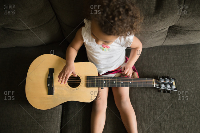 A little girl holds a guitar in her lap
