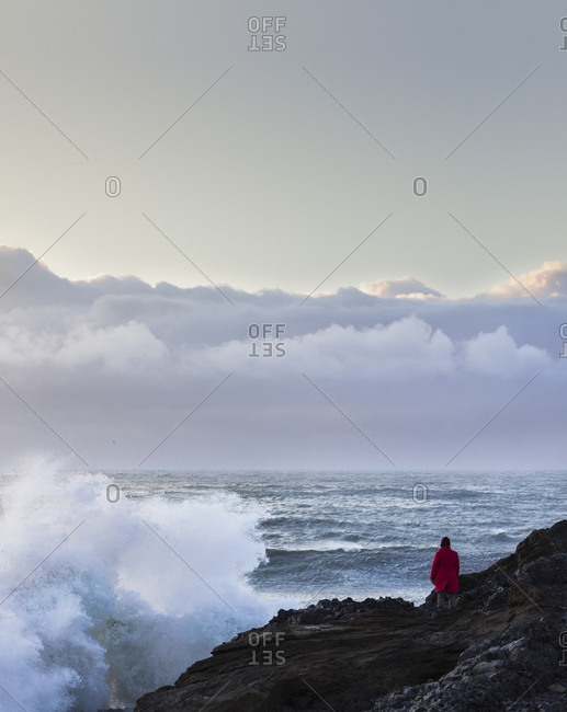 Person in a red coat watches waves crash against the volcanic coastline of Iceland