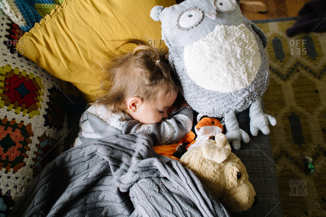 Little girl taking a nap with her stuffed animals on the couch