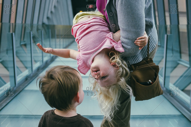 Child being held upside-down by parent looks at her sibling
