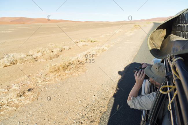 Man in a car looking through binoculars, Namib Naukluft Park, Namib Desert