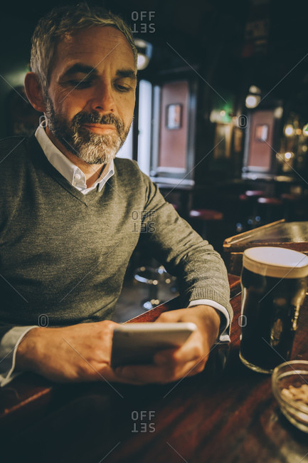 Portrait of man sitting at counter of a pub using smartphone