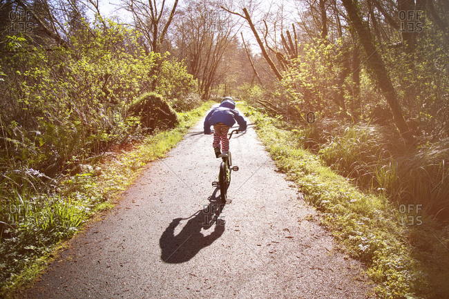 Child standing on bike seat on a sunny wooded path