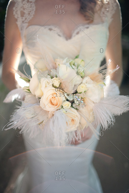 A bride holds her bouquet filled with feathers and roses