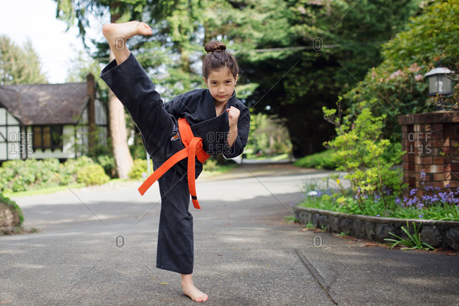 A girl wearing an orange belt practices a karate kick