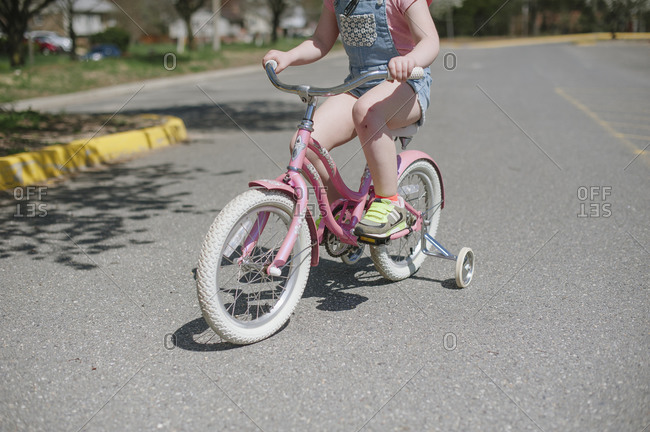 Closeup of a child riding a pink bicycle with training wheels