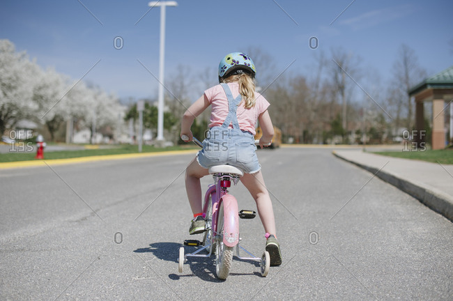 Back view of child riding a bicycle with training wheels in a school parking lot