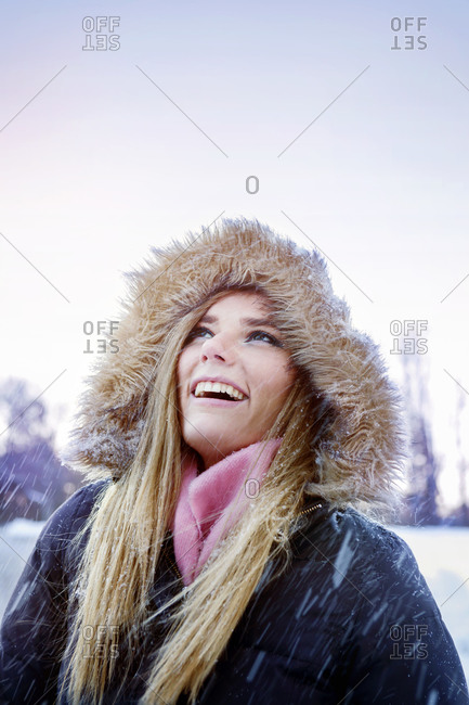 A woman in a fur lined jacket looks up at falling snow
