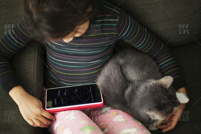 A little grill watches a video on a tablet while cuddling her cat