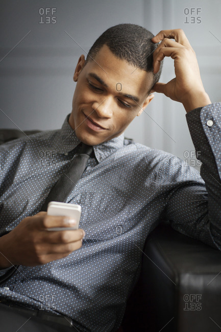 A young man sits on a leather couch and looks at his phone