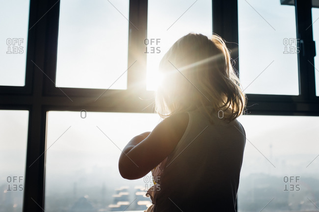Girl standing at sunlit window looking gout