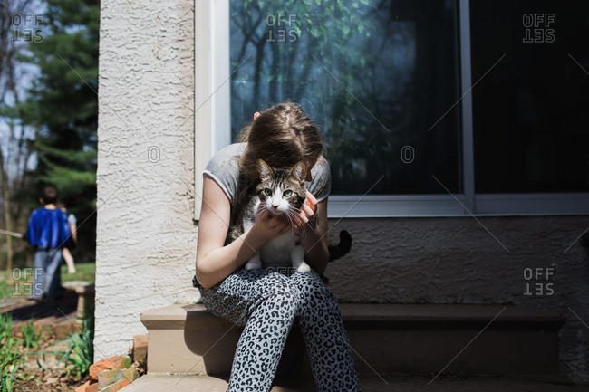 Teenage girl hugging her pet cat on her back steps