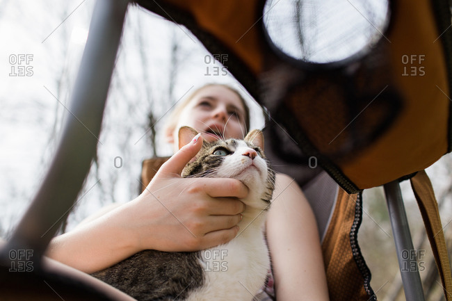 Teen girl in a camp chair scratches her cat\'s chin