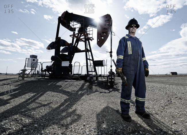 A man in overalls and hard hat at a pump jack in open ground at an oil extraction site