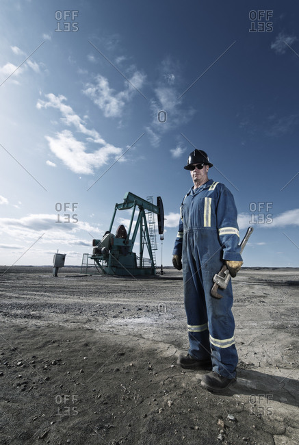 A man in overalls and hard hat at a pump jack in open ground at an oil extraction site