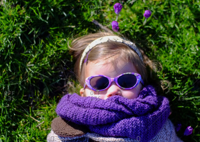 Young girl lying on grass with purple sunglasses surrounded by purple flowers