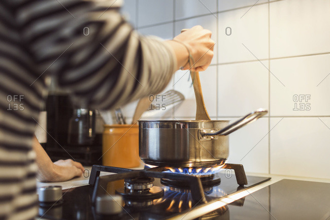 Woman holding spatula in sauce pan while cooking food on stove