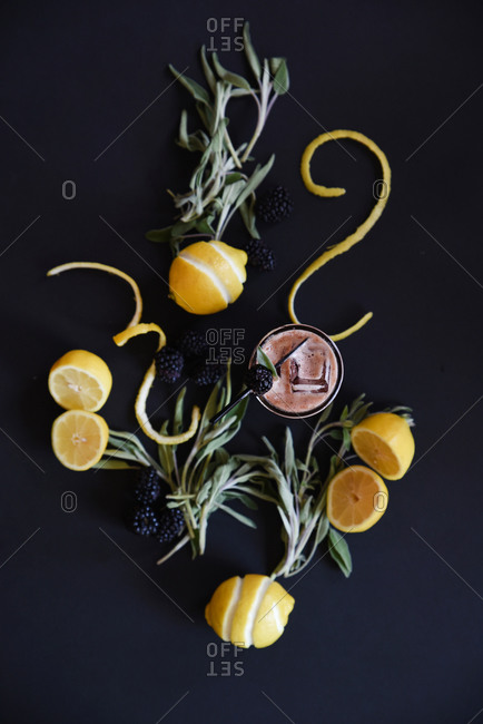 Ingredients for blackberry, lemon, sage, cocktail arranged on a black background