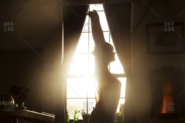 Backlit young woman stretching by window