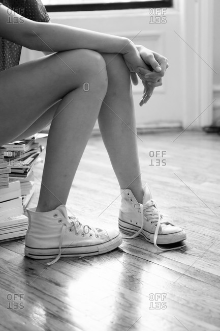 Young woman wearing high-top sneakers sitting on stack of books